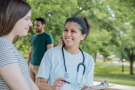 A public health nurse meets with a patient at an outdoor community health event.