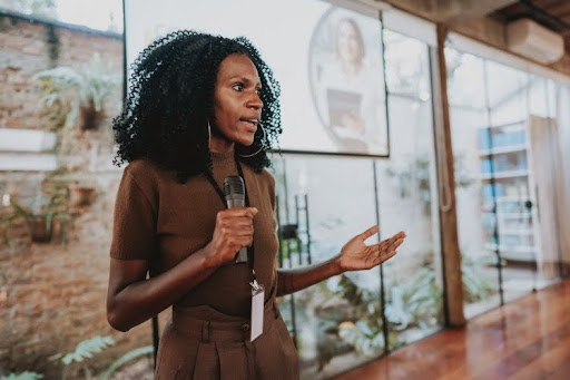 A training and development specialist holds a microphone and speaks in front of a projector screen in an office.