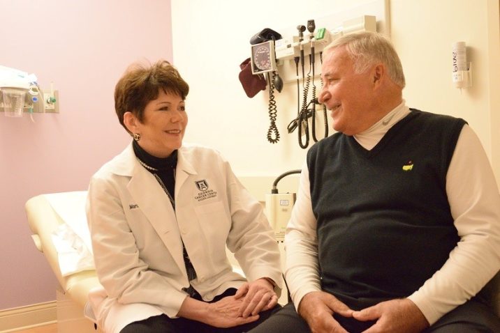 Woman in white coat sits talking with man in navy sweater
