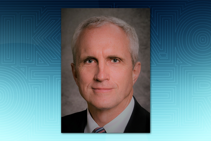Man in black suit and striped tie in front of a textured background