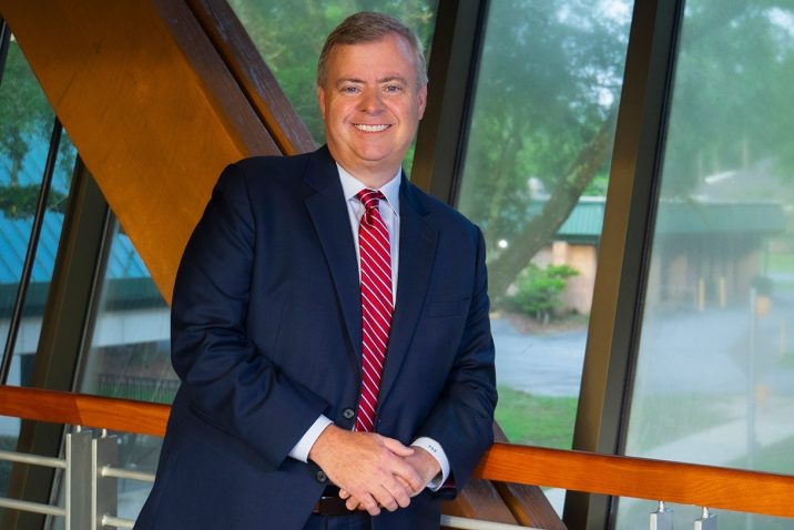 Man in blue suit and red tie leans against wooden beam