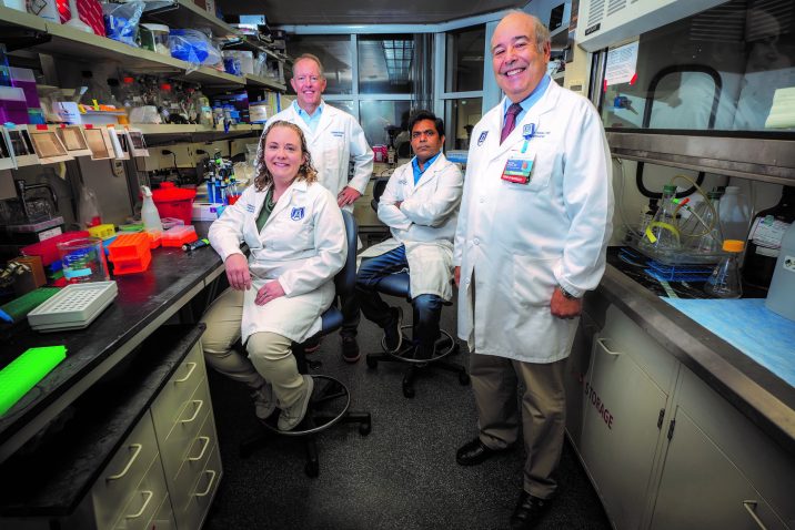 Four people in white coats stand in lab