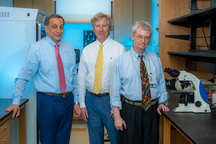 three men stand in a science lab