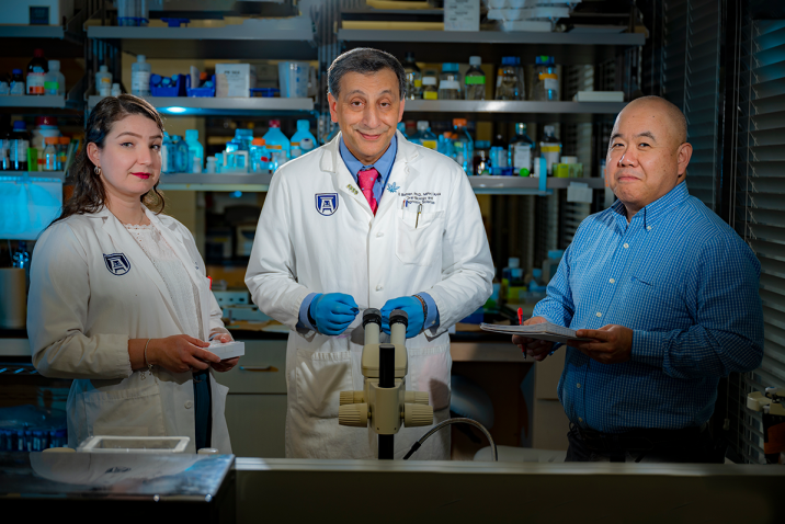 two men and a woman standing in a science lab smiling for the camera