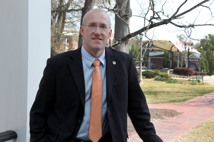 man in suit and tie leans against a railing outside
