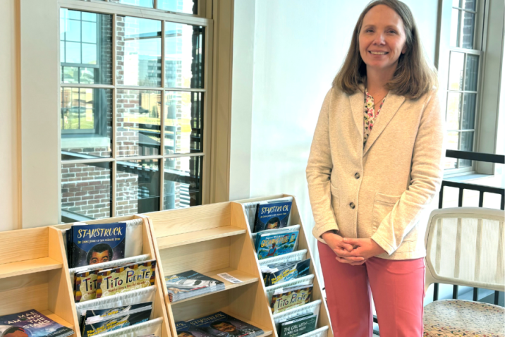 A woman stands next to bookshelves filled with children's books.