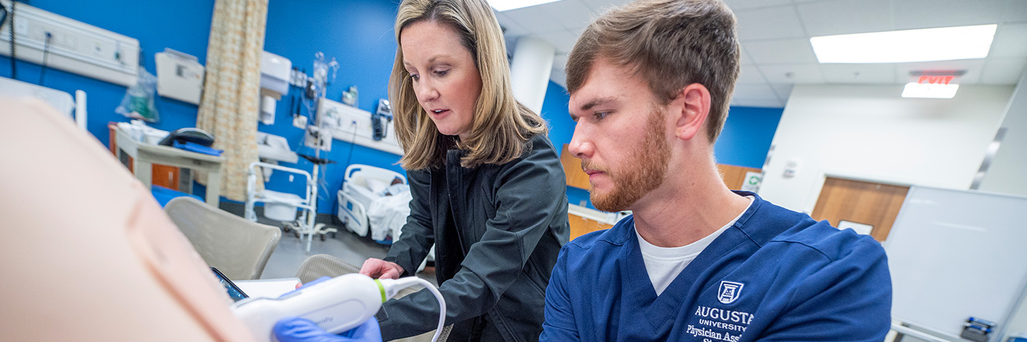 PA faculty works with student using ultrasound to practice lumbar punctures on task trainer model.