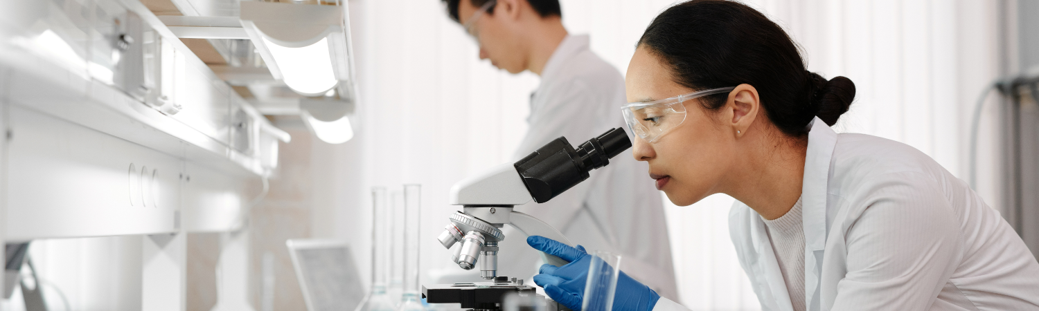 woman in lab looks through a microscope