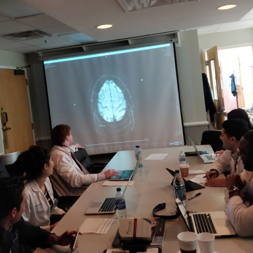 Residents sitting at a conference table looking at an image of a brain scan on a computer screen.