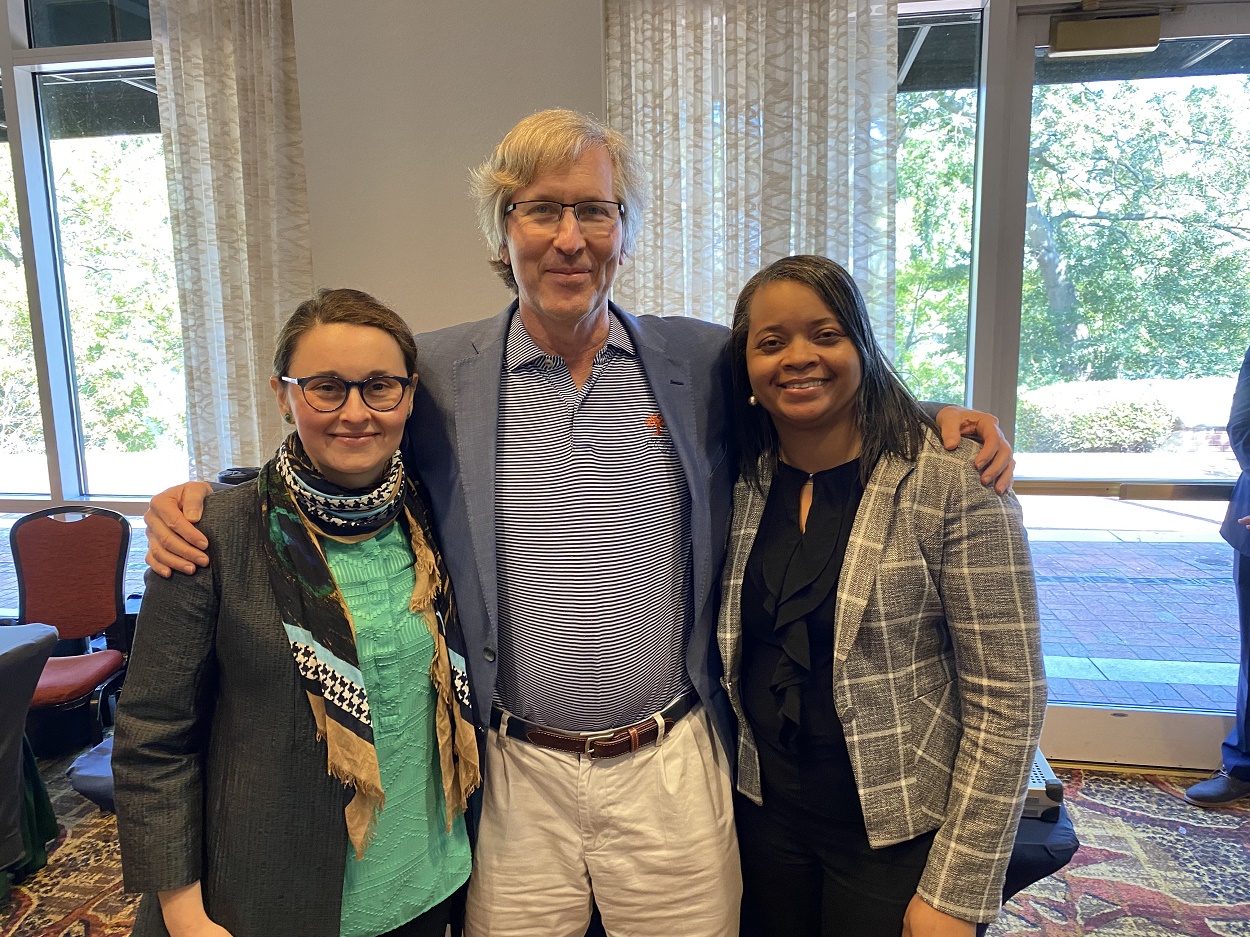 Man standing in the middle with his arms around the shoulders of 2 women colleagues .