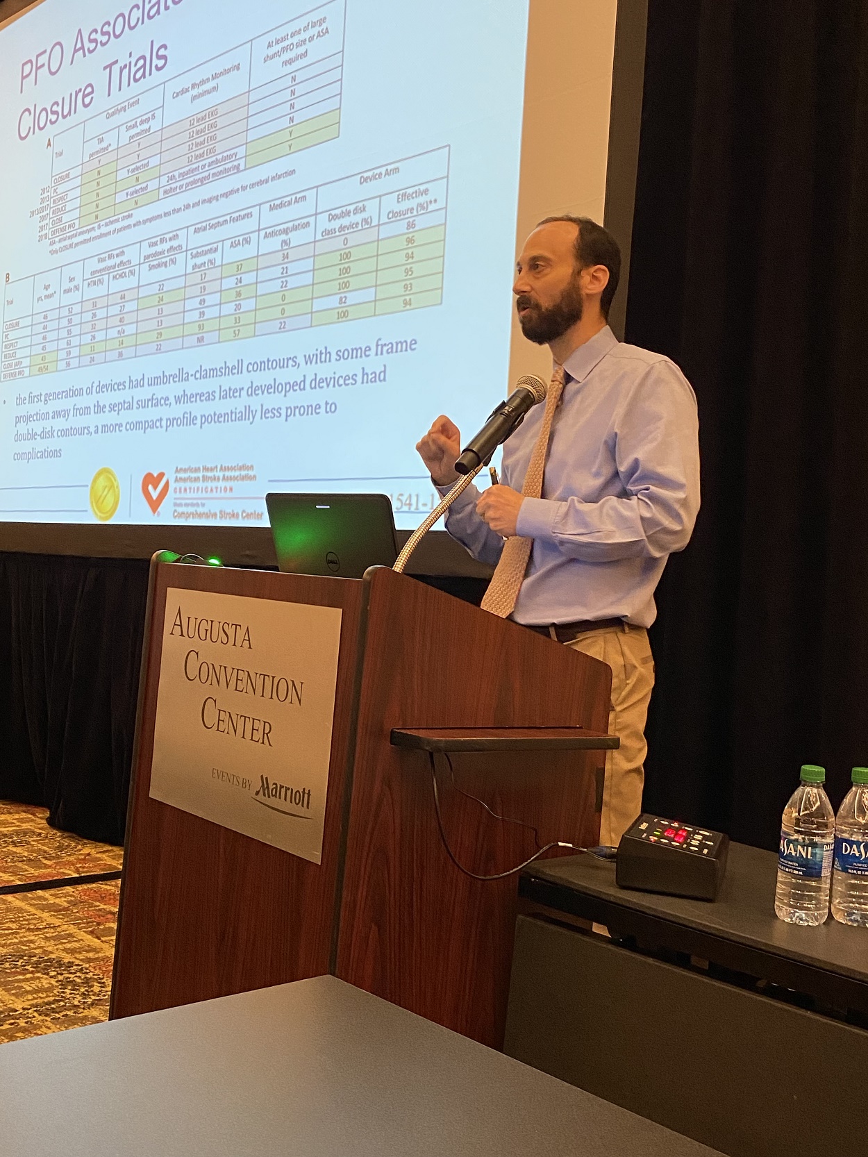 Man standing at a podium giving a talk with a screen behind him showing charted information
