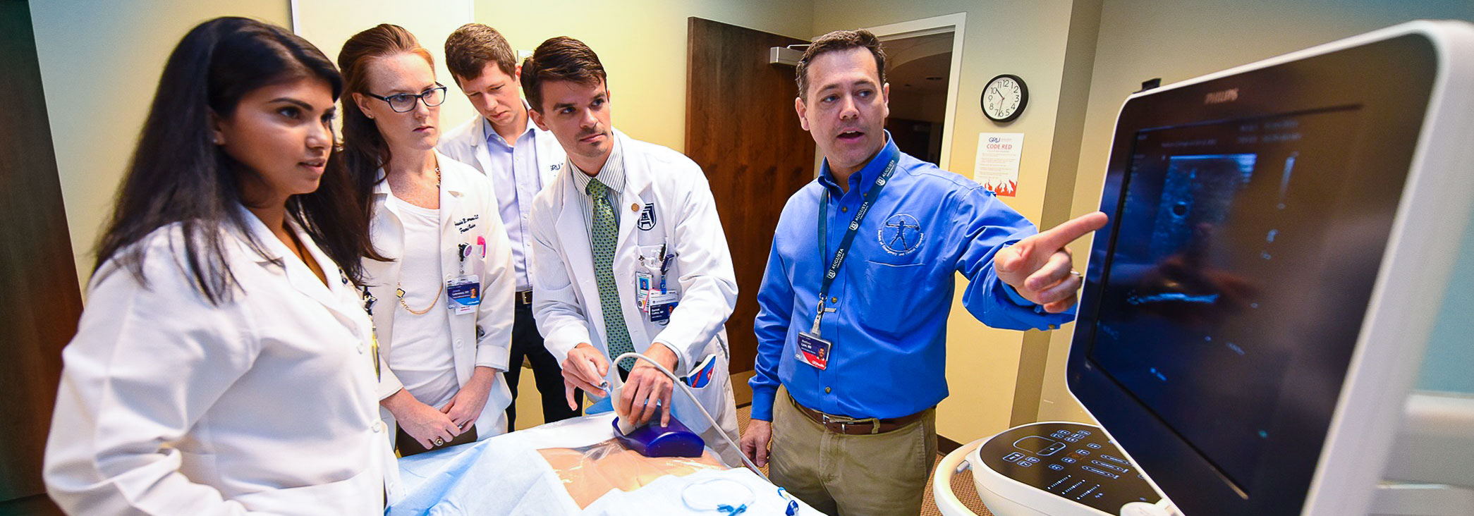man points to ultrasound machine and students look on