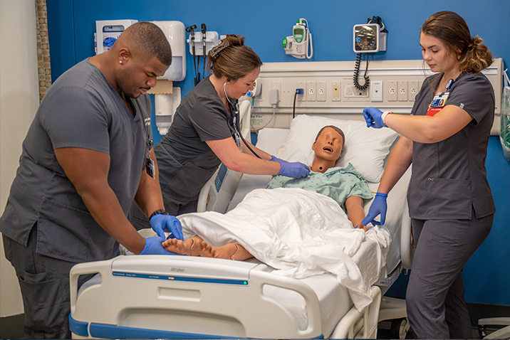 Graduate students performing vitals check on medical dummy