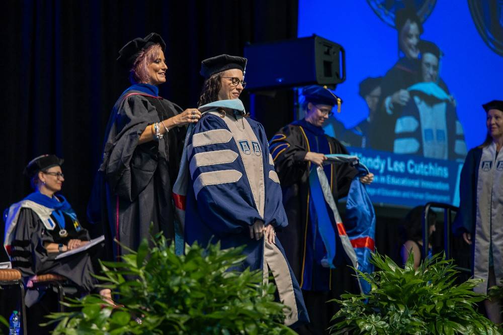 woman placing hood on student