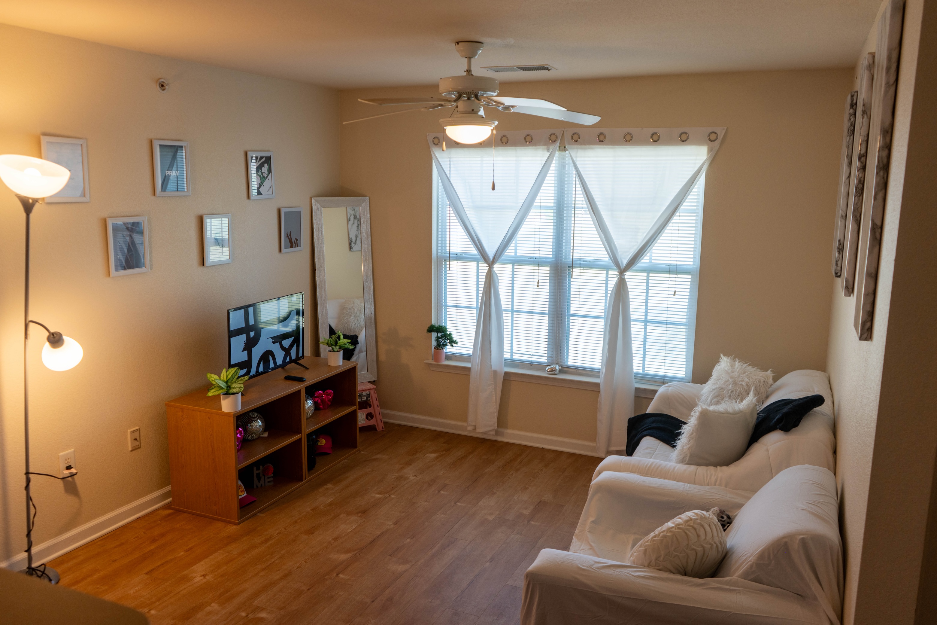 living room showing sofa and side chair facing TV set, wood floors, and large windows. 