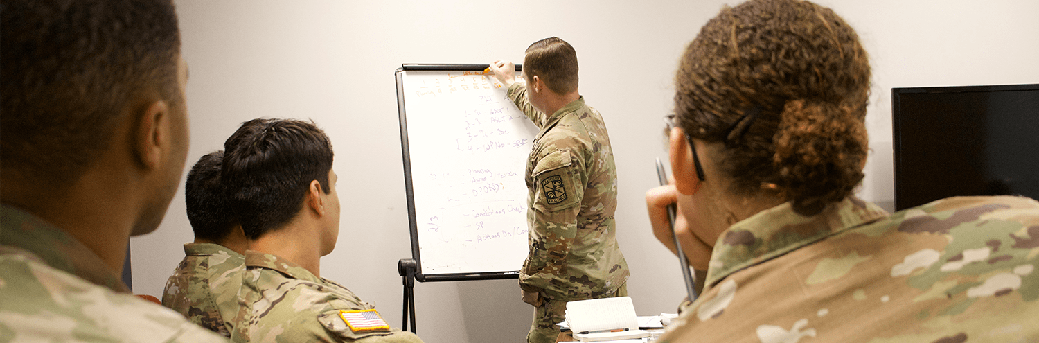 Back of cadets’ head as they watch an instructor give a lesson on a whiteboard