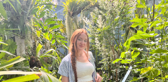 Woman stands in front of trees for photo.