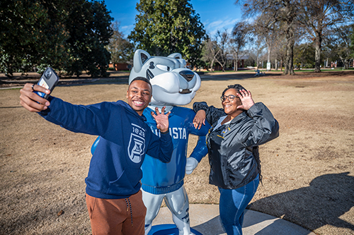 Two students taking a selfie with the Augustus status on campus